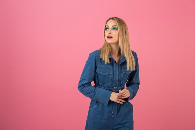 Young pretty cute woman in stylish outfit in pink sweater and sunglasses isolated on pink studio background