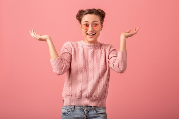 젊은 예쁜 분홍색 스웨터와 분홍색 스튜디오 배경에 고립 된 선글라스에 재미 있은 얼굴로 웃는 여자를 종료