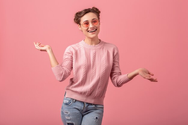 Young pretty exited laughing woman with funny face in pink sweater and sunglasses in spring style trend isolated on pink studio background