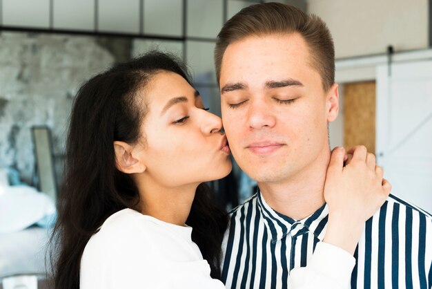 Young pretty female kissing boyfriend on cheek