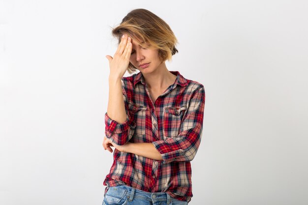 Young pretty funny emotional woman in checkered shirt posing isolated on white studio wall, showing headache gesture