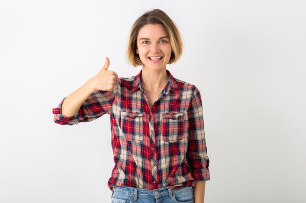 Young pretty funny emotional woman in checkered shirt posing isolated on white studio wall, showing thumb up gesture