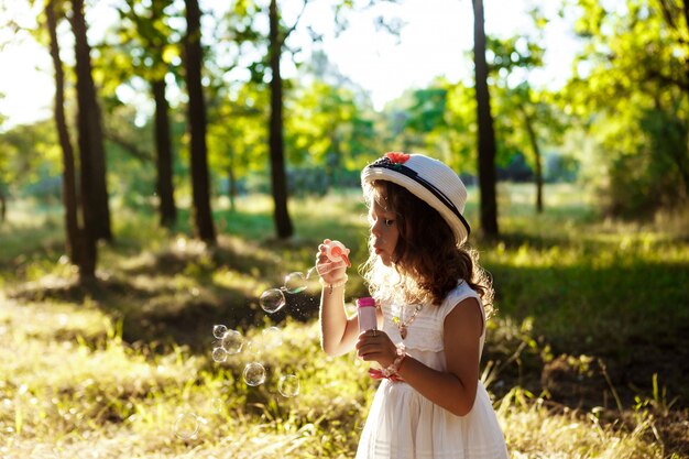 Young pretty girl blowing bubbles, walking in park at sunset.