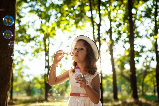 Young pretty girl blowing bubbles, walking in park at sunset.