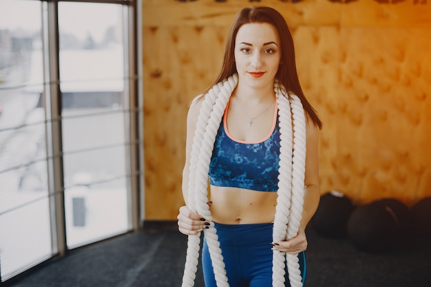 Foto gratuita giovane e bella ragazza in una tuta sportiva blu è impegnata nello sport in palestra