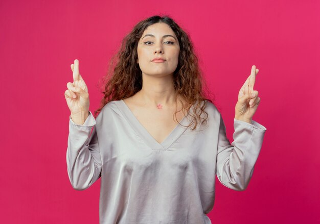 young pretty girl crossing fingers isolated on pink wall