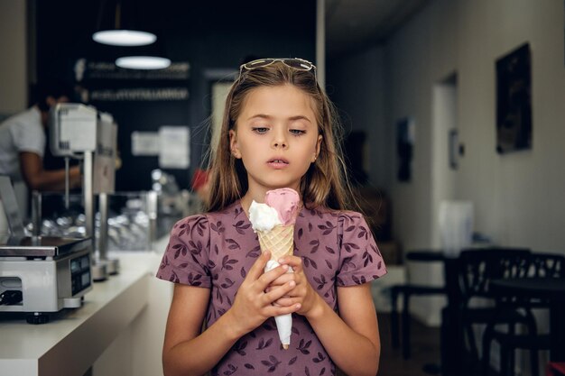 カフェでアイスクリームを食べて、ドレスを着た若いかわいい女の子。