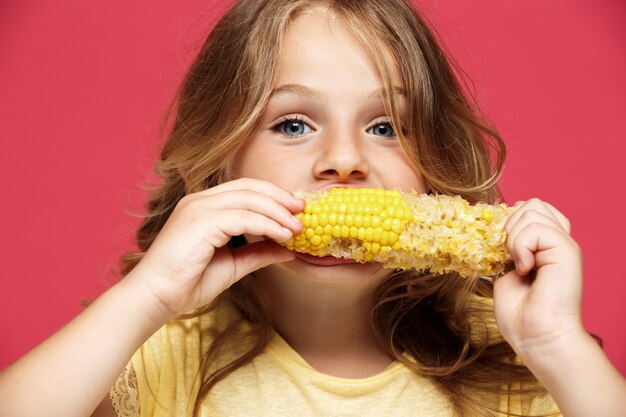 Молодая красивая девушка ест кукурузу над розовой стеной
