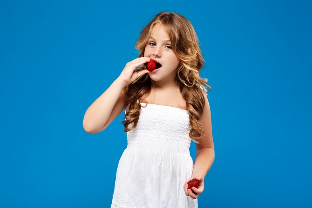 Young pretty girl eating strawberry over blue wall