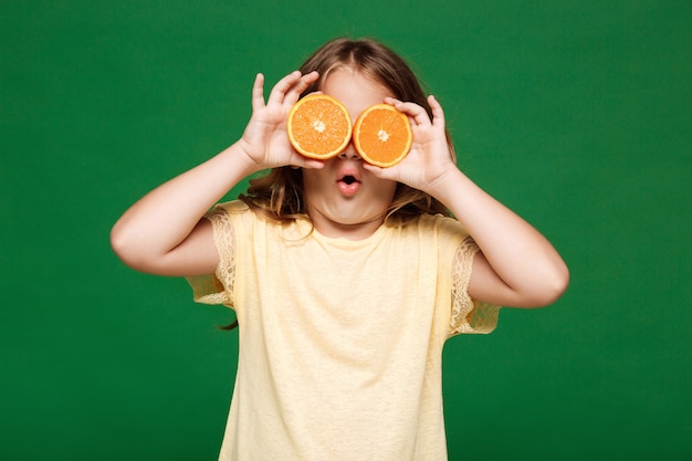 Молодая красивая девушка, скрывая глаза с апельсинами над зеленой стеной