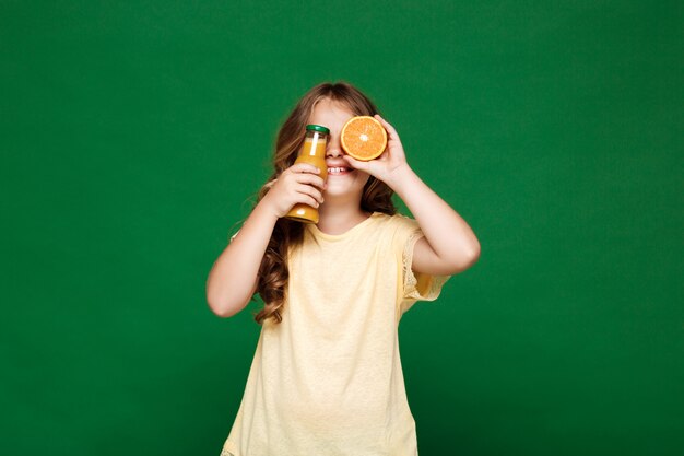 Young pretty girl hiding eyes with oranges over green wall