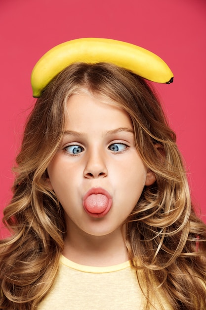 Young pretty girl holding banana on head over pink wall