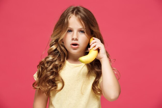ピンクの壁に電話のようなバナナを保持している若いきれいな女の子