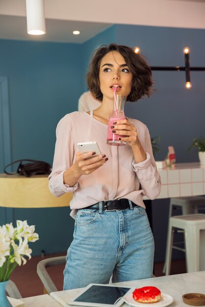 Young pretty girl holding mobile phone and drinking smoothie