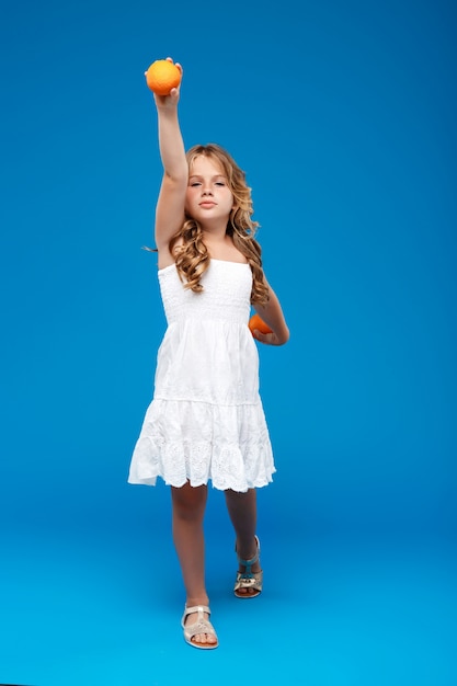 Young pretty girl holding oranges over blue wall