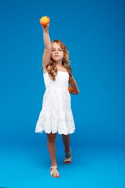 Young pretty girl holding oranges over blue wall