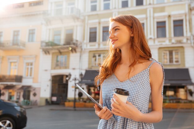 PCタブレットと一杯のコーヒーを保持している若いきれいな女の子