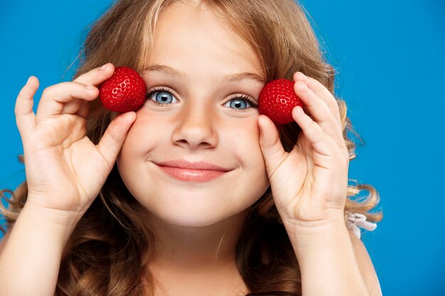 Young pretty girl holding strawberry over blue wall