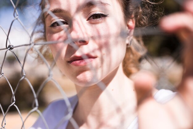 Young pretty girl looking through metal grid