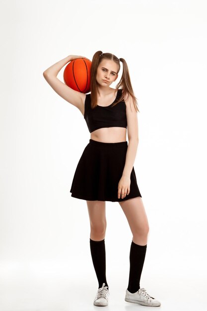 白い背景の上にバスケットボールでポーズをとって若いかわいい女の子