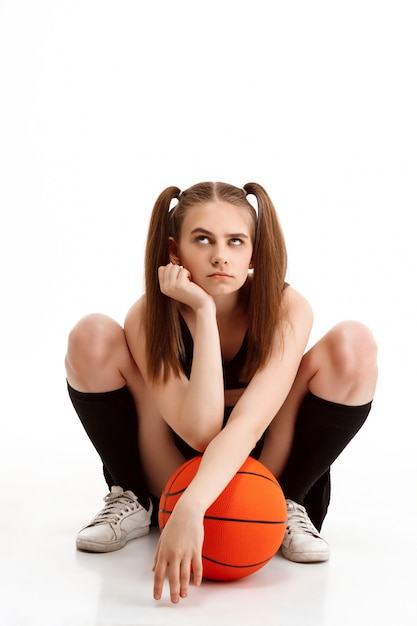 Молодая милая девушка представляя с баскетболом над белой стеной