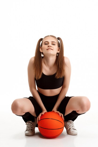 Young pretty girl posing with basketball over white wall