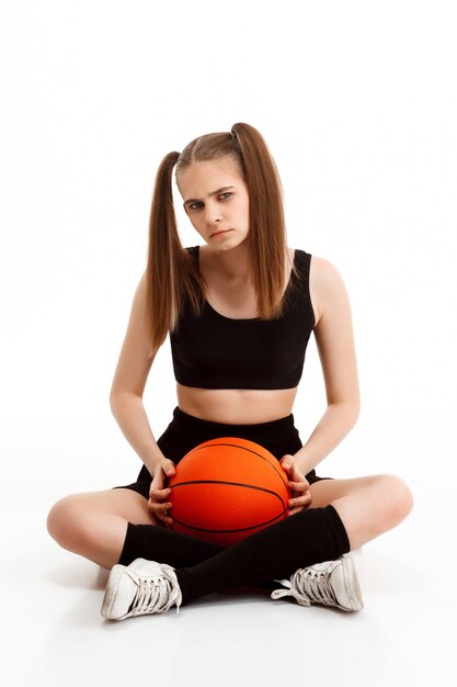 Young pretty girl posing with basketball over white wall