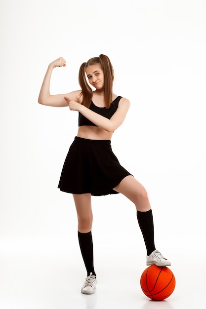 Young pretty girl posing with basketball over white wall