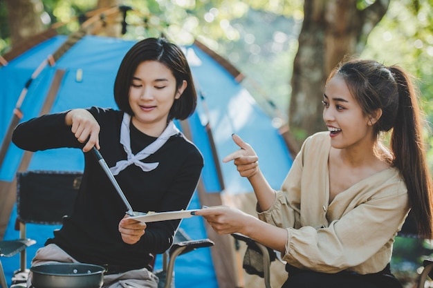 Young pretty girl put an egg on pan while camping with her friends cooking easy meal in nature park They are enjoy to discussion and laugh with fun together copy space