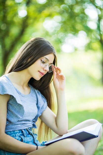 Young pretty girl reading book at park in summer sunset light