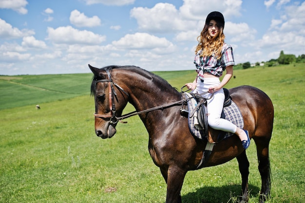 Young pretty girl riding a horse on a field at sunny day