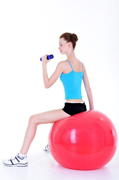 Young pretty girl sitting on the fitball and doing exercise with dumbbells