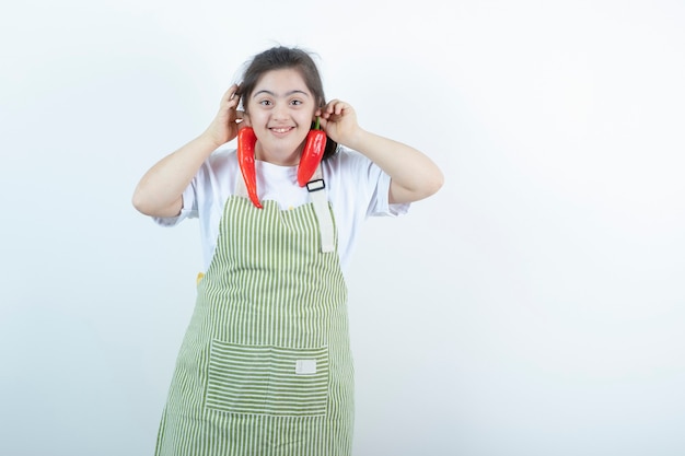 Free photo young pretty girl standing in checkered apron and holding two red hot chili peppers .