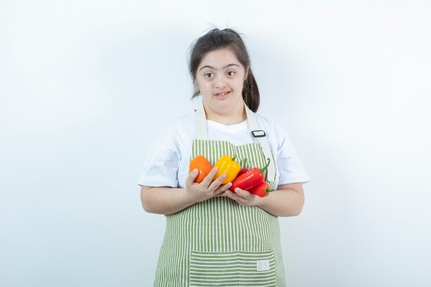 Young pretty girl standing in checkered apron and holding vegetables .