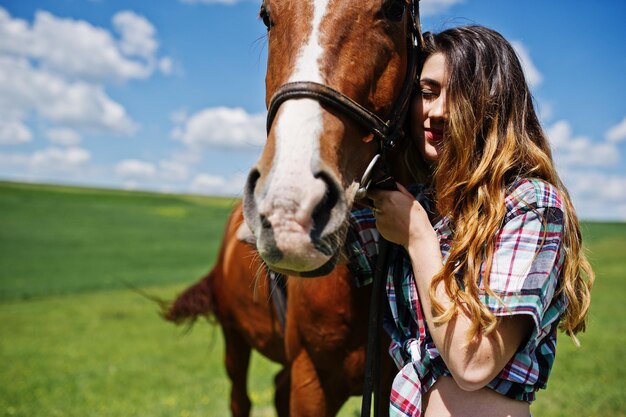 Молодая красивая девушка остается с лошадью на поле в солнечный день