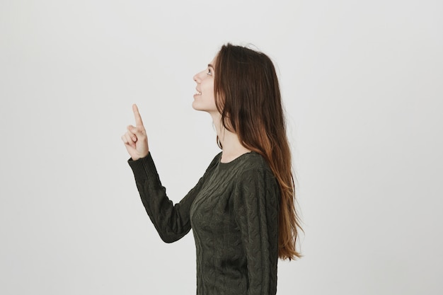 Young pretty girl in sweater, standing profile, raise head and pointing up