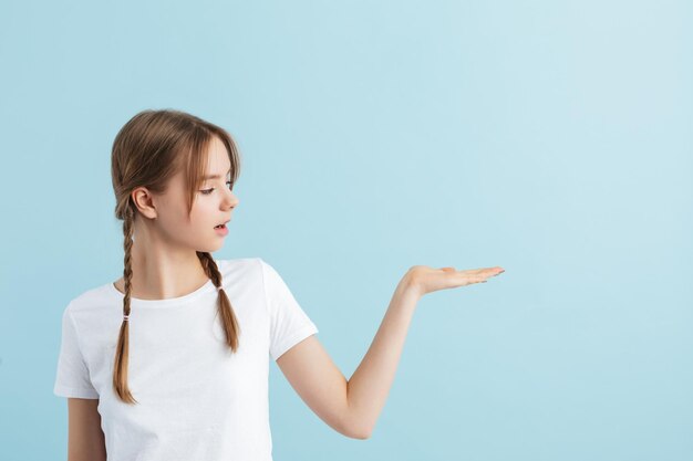 Young pretty girl with two braids in white tshirt dreamily looking aside showing invisible copyspace over blue background isolated