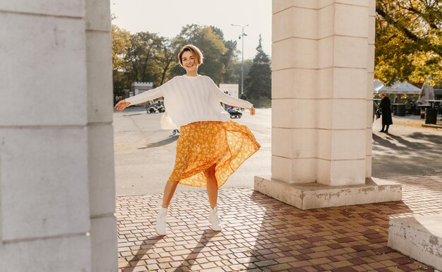 Young pretty happy smiling woman in yellow printed dress and knitted white sweater