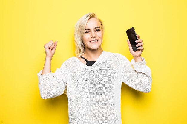 Young pretty lady woman girl in white sweater uses smartphone on yellow