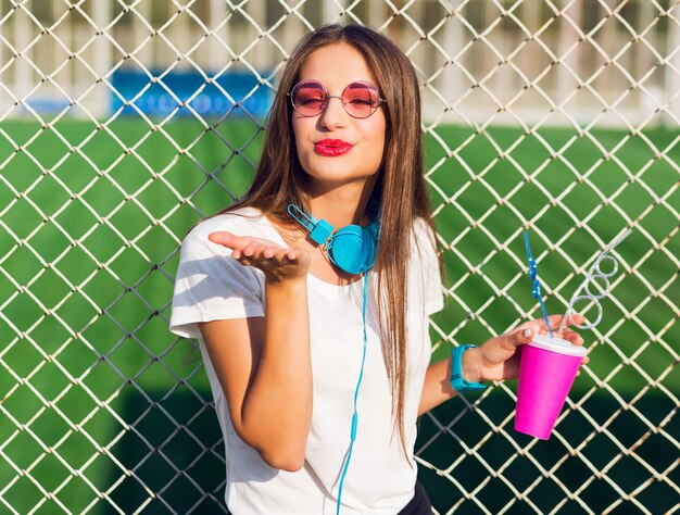 Young pretty lovely hipster woman posing with cup of healthy juice, listening favorite music