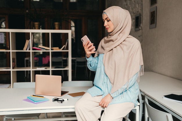 Giovane donna musulmana piuttosto moderna in hijab che lavora nella stanza dell'ufficio, istruzione online