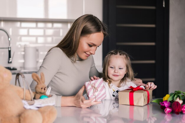 Young pretty mother and daughter with gifts box in the kitchen