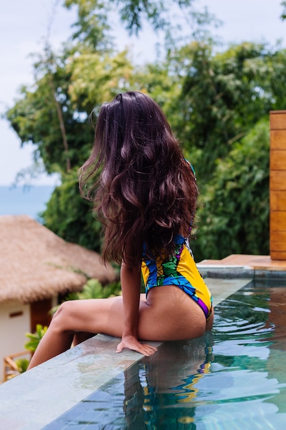 Молодая довольно позитивная счастливая стройная женщина в красочном купальнике на роскошной удивительной вилле отеля, наслаждаясь прекрасным днем на отдыхе в Таиланде