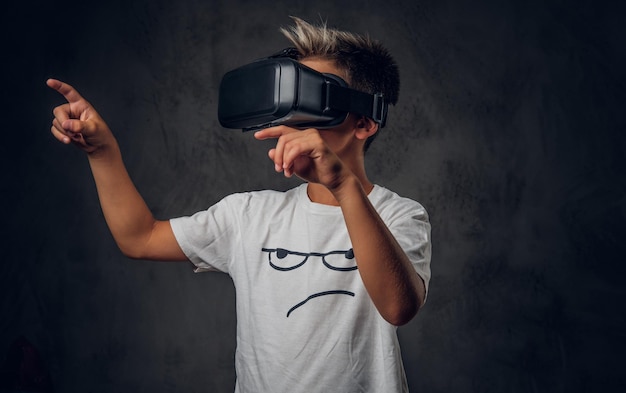 Young pretty schoolboy is playing virtual video game wearing special goggles.