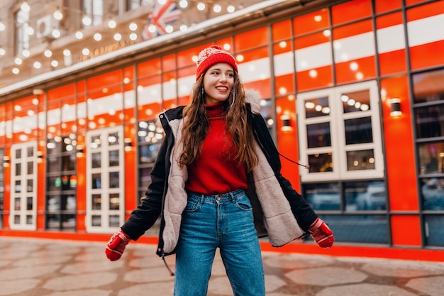 Free photo young pretty smiling happy woman in red mittens and knitted hat wearing winter coat walking in city street, warm clothes