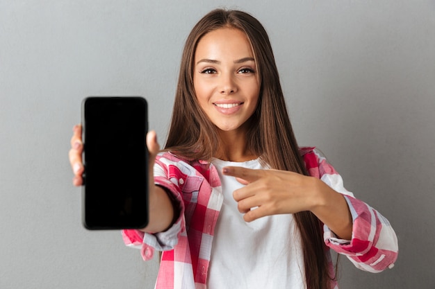 Young pretty smiling woman pointing with finger on phone screen
