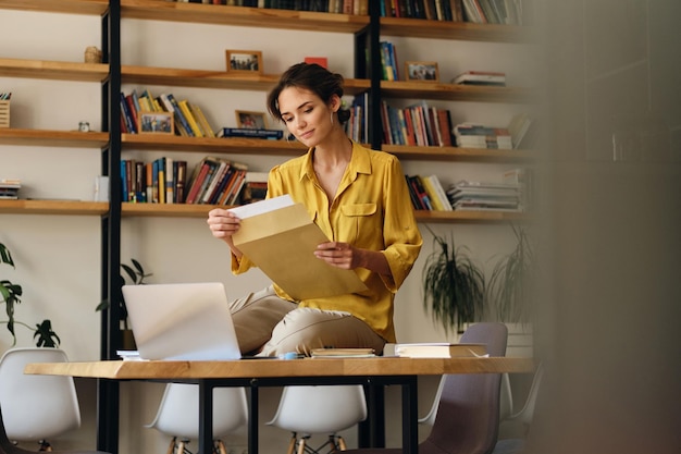 현대 사무실에서 꿈꾸는 동안 책상에 서류와 노트북으로 앉아 노란색 셔츠에 젊은 예쁜 웃는 여자