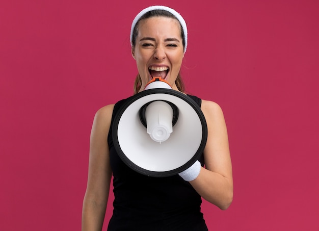 Young pretty sporty girl wearing headband and wristbands shouting in loud speaker 