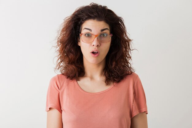 Young pretty stylish woman in glasses, curly hair, shocked, surprised face expression, funny emotion, isolated, pink t-shirt