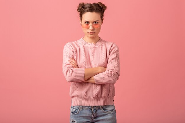 Young pretty thinking woman having a problem, looking down in pink sweater and sunglasses isolated on pink studio background